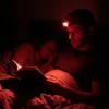 un homme lit un livre dans son lit, éclaré par une lampe frontale rouge pendant que sa femme dort